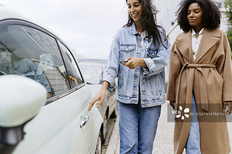 快乐的年轻女人和朋友用遥控钥匙解锁汽车图片素材