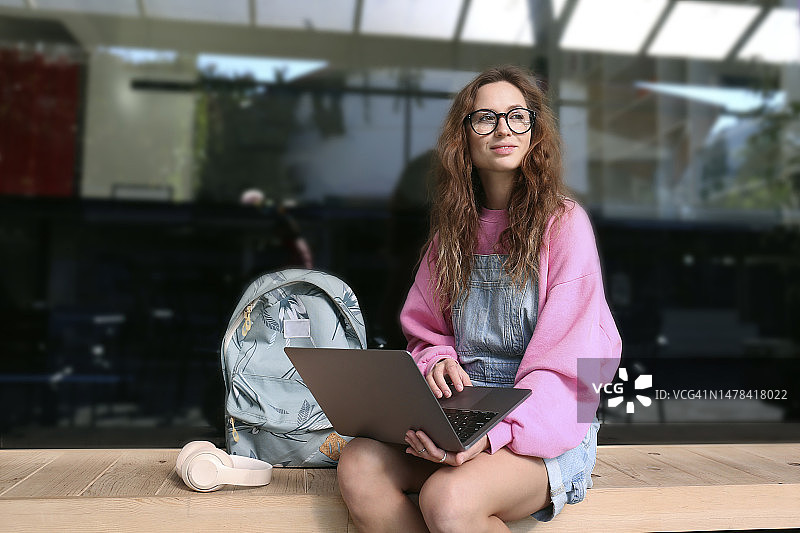 沉思的学生携带笔记本电脑和背包坐在长椅上图片素材