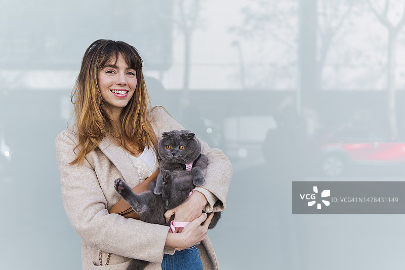 快乐的女人抱着猫站在墙前图片素材