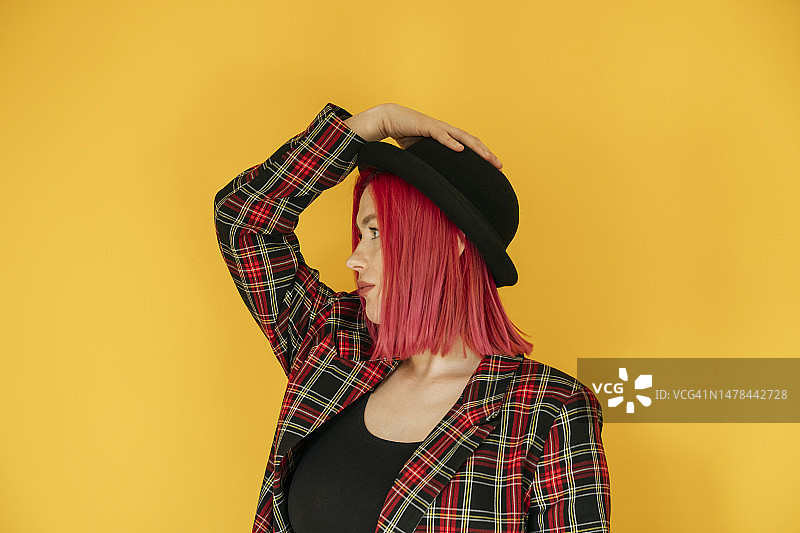 戴着圆顶礼帽的沉思女人站在黄色背景前图片素材