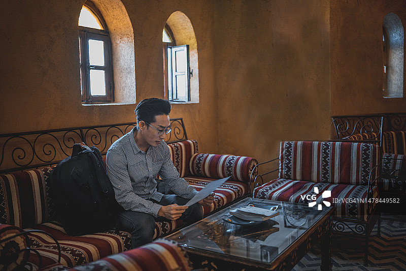 在撒哈拉沙漠度假村沙发上填写旅行登记表的中国亚洲中年男人独自旅行图片素材