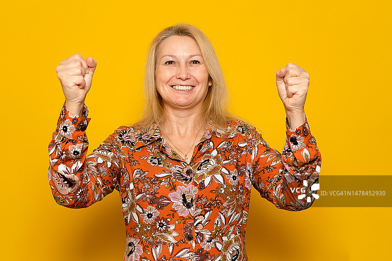 快乐的白人成功女性，身穿图案连衣裙，举手欢庆图片素材