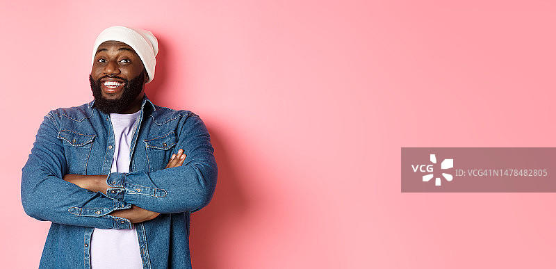 戴着无檐小便帽和牛仔衬衫的快乐黑人男子，正在看图片素材