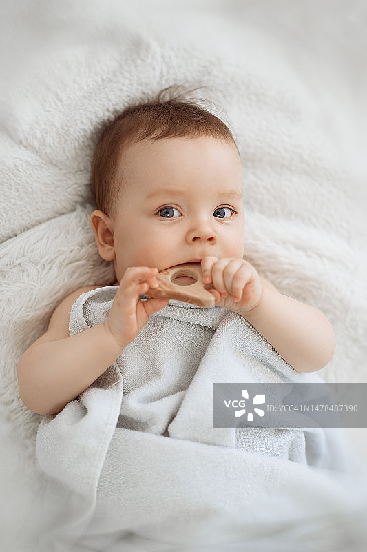可爱有趣的小宝宝在用木制磨牙器后在床上休息图片素材