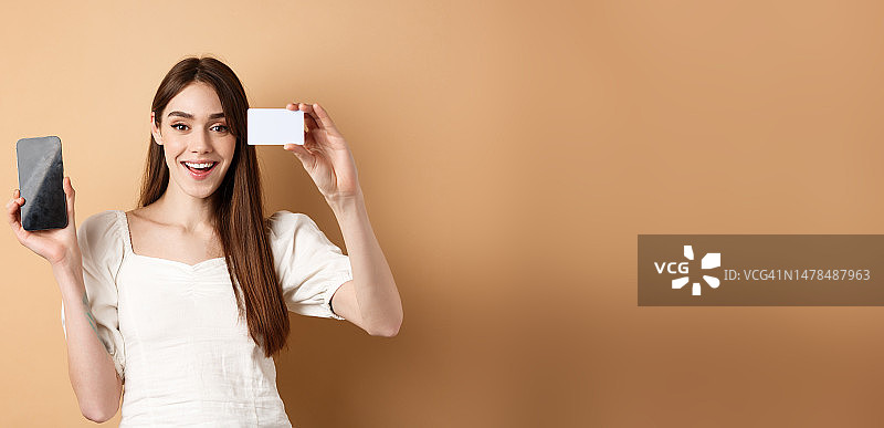 快乐的年轻女人展示塑料信用卡和空白手机图片素材