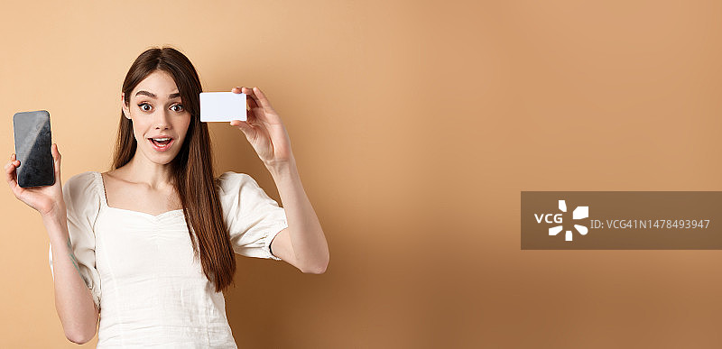 兴奋的女孩展示银行信用卡和空白手机图片素材