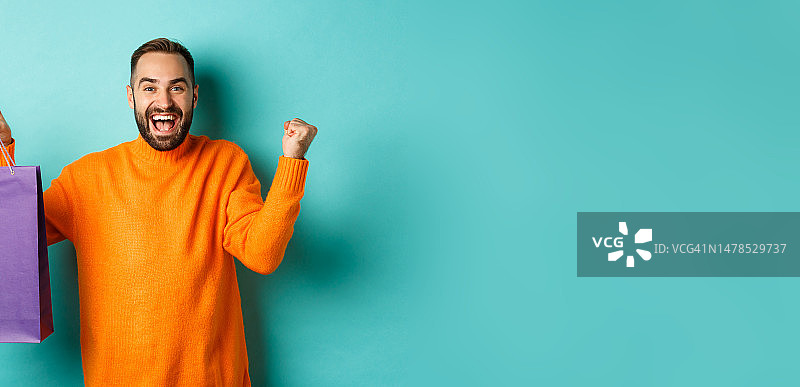 快乐的男人拿着紫色购物袋，因获得折扣而欢欣鼓舞图片素材