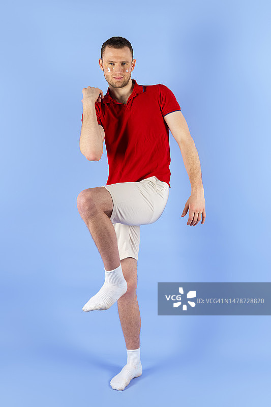 身穿红色POLO衫、贴着眼膜的年轻帅气健康男子全身照，蓝色背景图片素材