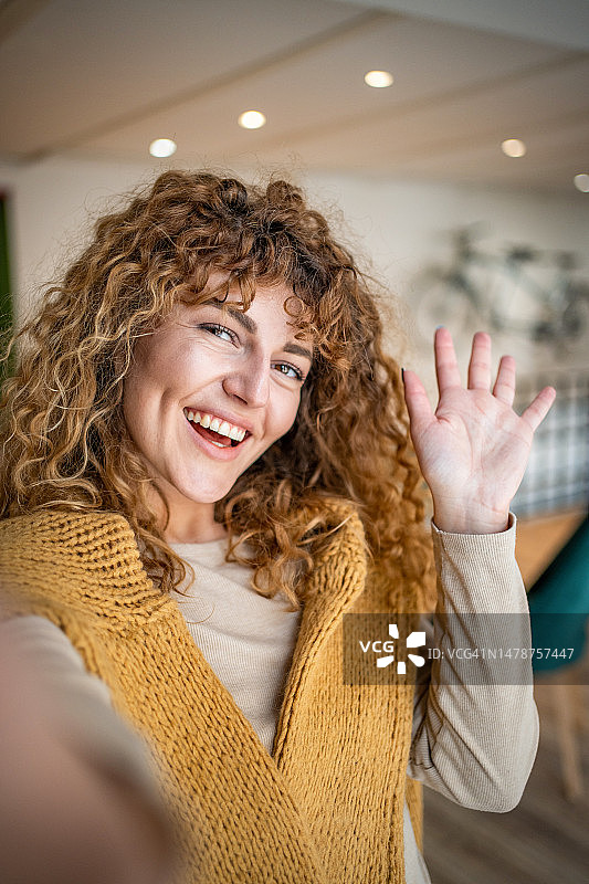 一位有着卷发的年轻漂亮女孩在最喜欢的咖啡店自拍图片素材