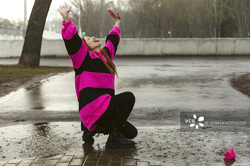 穿着亮紫色毛衣的女人玩着折纸。下雨天，享受生活图片素材