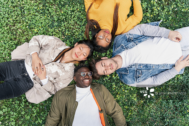 快乐的非裔美国男人与一群多种族年轻朋友一起躺在草地上图片素材