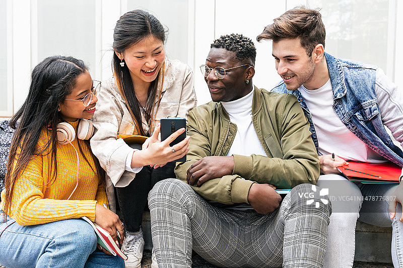 大学生朋友们坐在一起用手机分享社交媒体内容图片素材