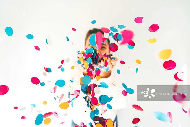 对着镜头吹起五彩纸屑的美丽女人，广角，节日概念图片素材