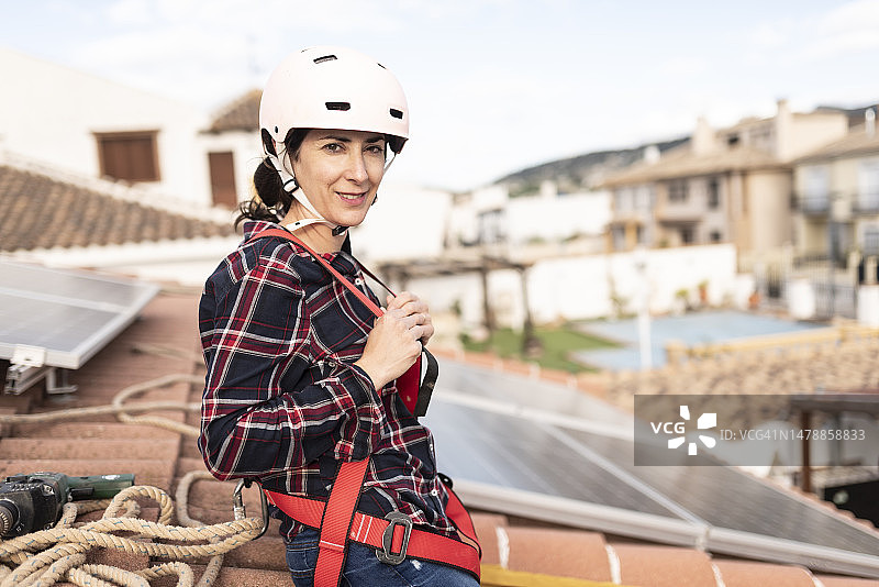 头戴头盔和安全带，从事垂直作业的专家正在安装和维护太阳能电池板，对着镜头微笑图片素材