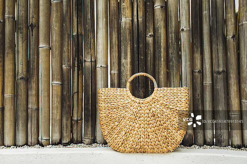 竹墙背景上的草编沙滩包图片素材