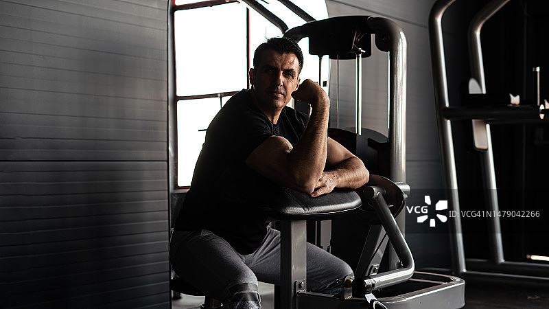 肌肉男坐在健身房展示二头肌，水平健身照图片素材