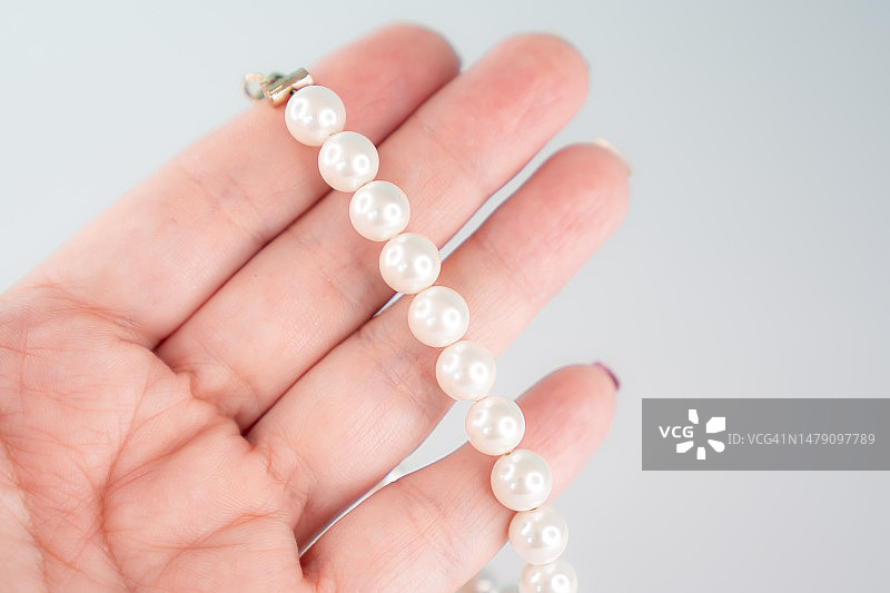 女性手指间拿着珍珠手链图片素材