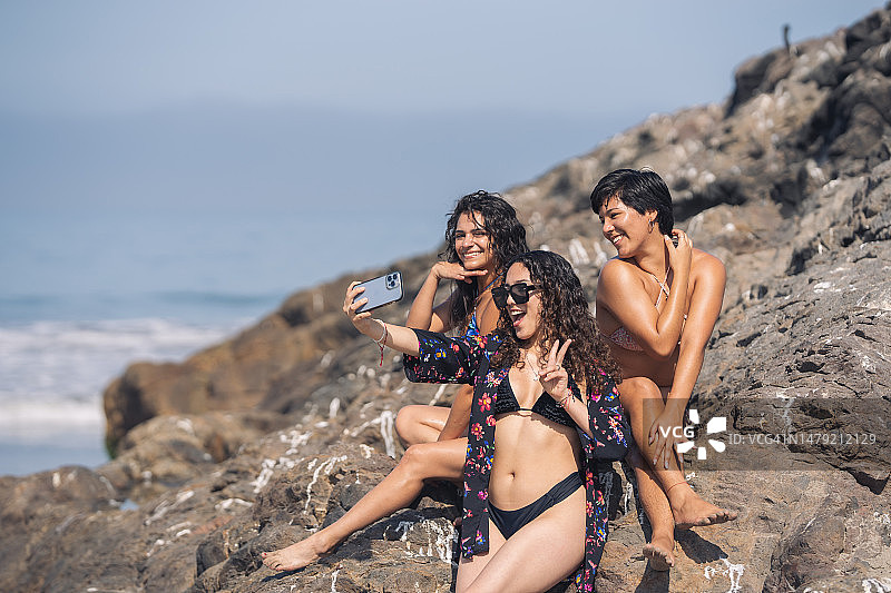 朋友们坐在海滩的岩石上自拍图片素材