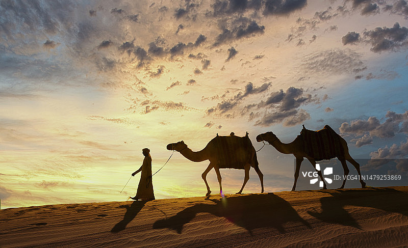 沙漠中与骆驼同行的阿拉伯男人图片素材