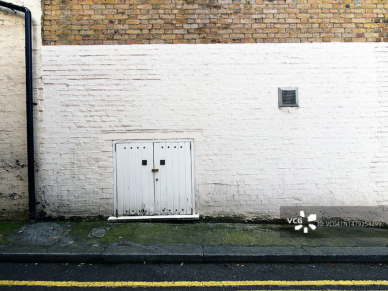 英国伦敦的风化棕色砖墙和白色涂漆墙面、混凝土人行道与黄色标线沥青路面图片素材
