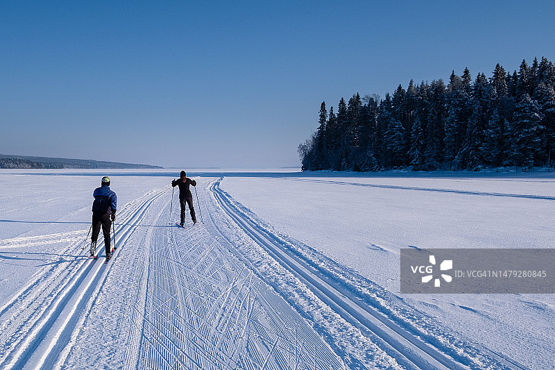 在芬兰中部卡亚尼凯努区，母亲和十几岁的儿子在乌卢湖冰冻的公共滑雪道上越野滑雪图片素材