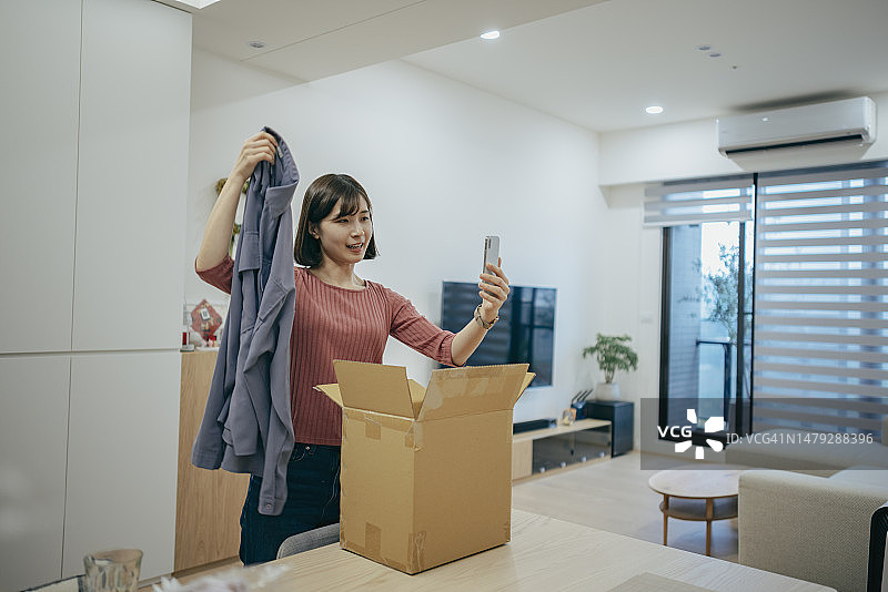 亚洲女人在家拆快递，用手机和朋友视频通话图片素材