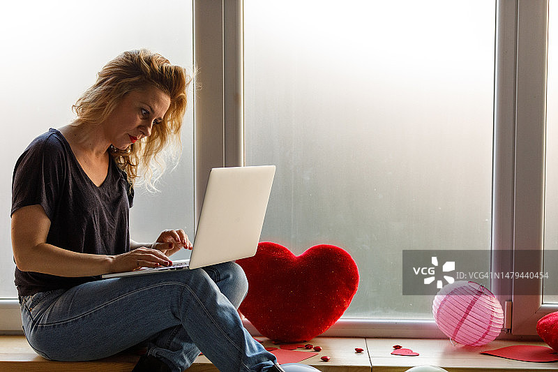 坐在窗台上用笔记本电脑，思念爱人的女人图片素材