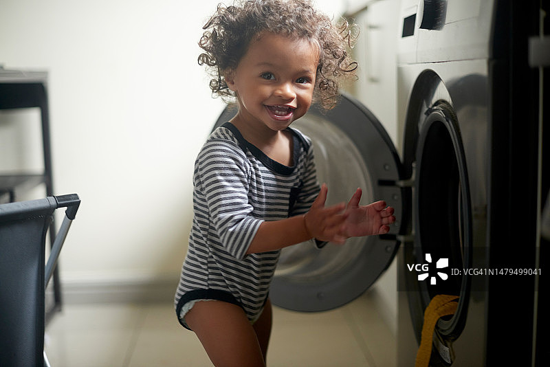 快乐的宝宝在洗衣机旁玩耍，在洗衣房体验自由乐趣图片素材