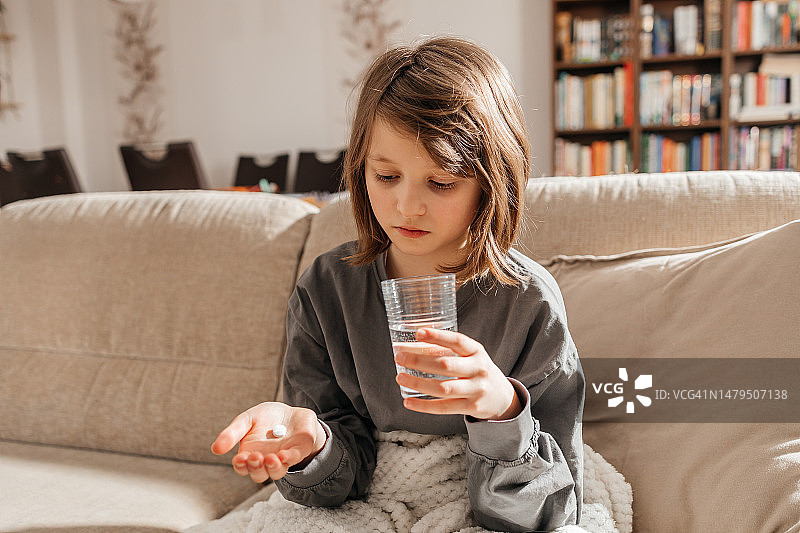 坐在沙发上服用药物或维生素以增强免疫力的少女图片素材