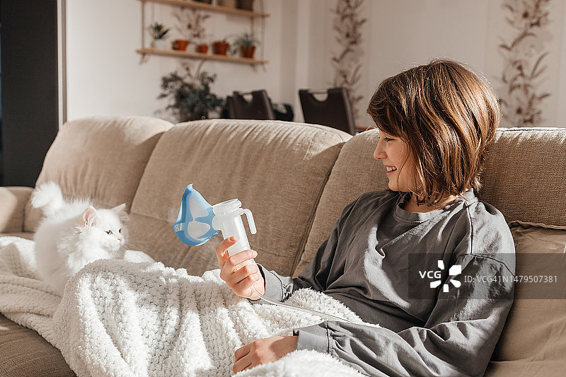 女孩坐在客厅沙发上，用雾化器吸入药物，居家治疗图片素材
