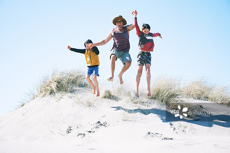 父亲和孩子们在沙丘上跳跃图片素材