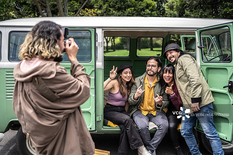 年轻男人在复古迷你货车里给朋友拍照图片素材