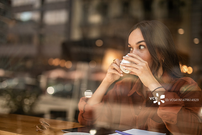 年轻女子坐在咖啡馆的窗边，享受美好的一天图片素材