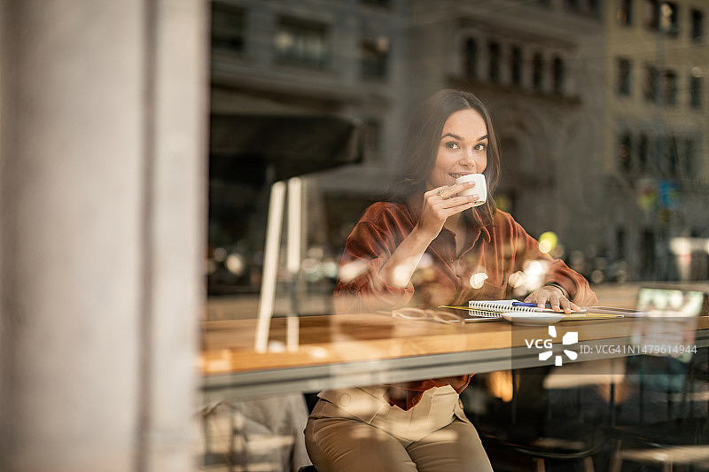 年轻女子坐在咖啡馆的窗边，享受美好的一天图片素材