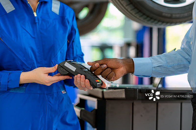 在汽车修理店检查完所有维修项目后，女机械师收到顾客的非接触式付款。图片素材