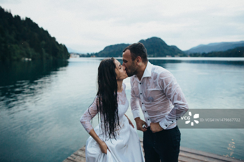 在潮湿的衣服中在码头上接吻的新婚夫妇图片素材