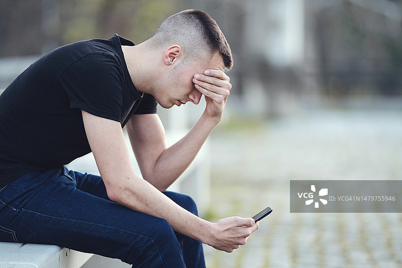 悲伤的年轻人坐在公园长椅上，用手捂脸图片素材