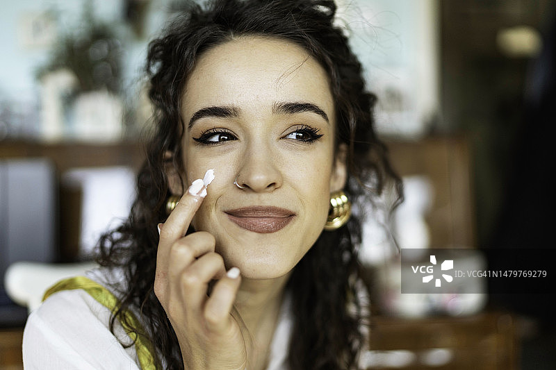 美丽的年轻女人在脸上涂抹保湿霜。皮肤护理和美容概念图片素材