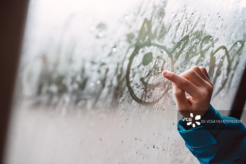 女孩在车内用手指在冷凝的车窗上绘画的特写图片素材