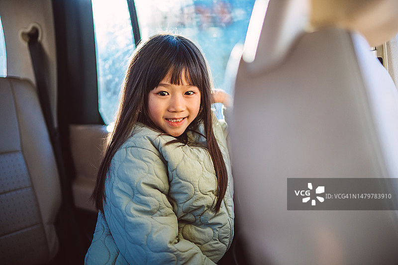坐在汽车后座，对着镜头快乐微笑的可爱女孩图片素材