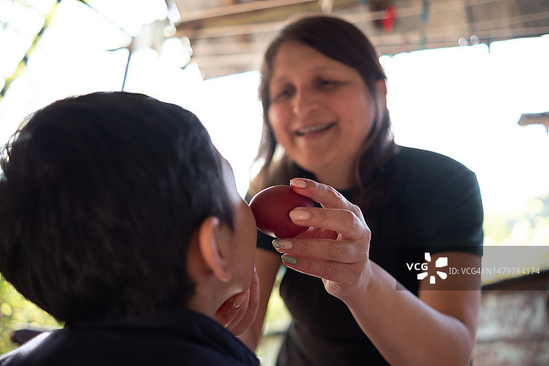 年轻快乐的女人用红鸡蛋擦拭小孩的脸颊，祈求健康图片素材