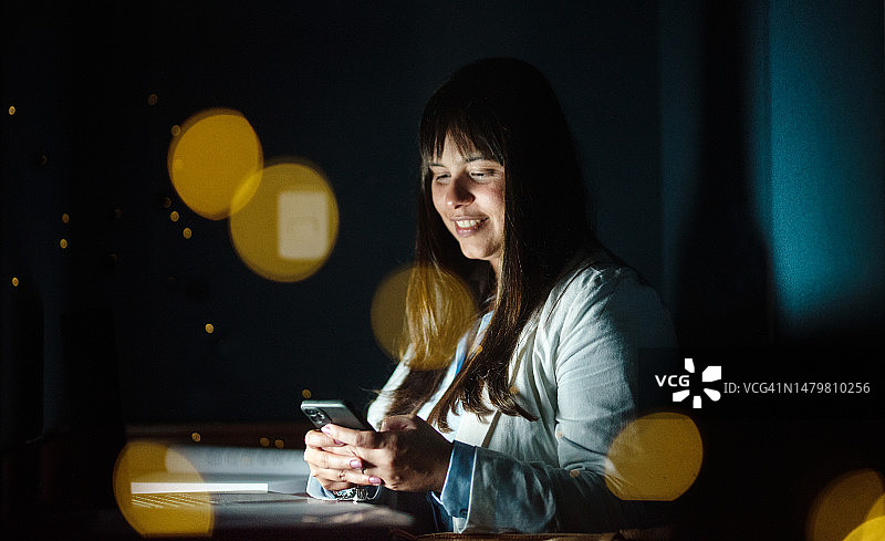 在办公室深夜工作的女商人用手机发短信图片素材