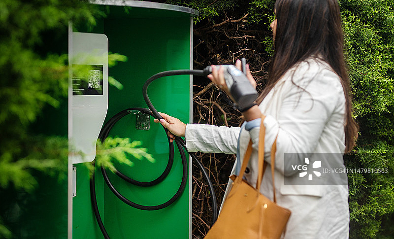 女商人将充电器挂在汽车充电站上图片素材