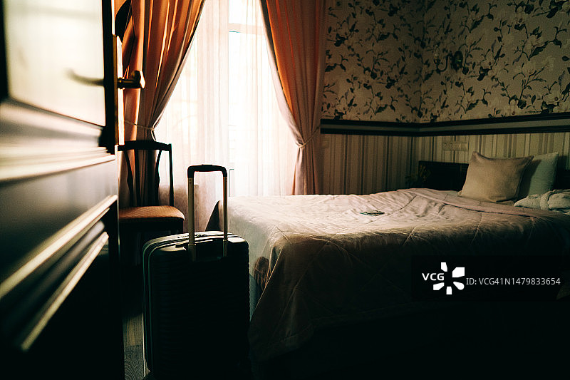 酒店内的单人小黑屋，带拉杆的行李箱，铺着床罩的床，窗帘。商务旅行或单人度假图片素材