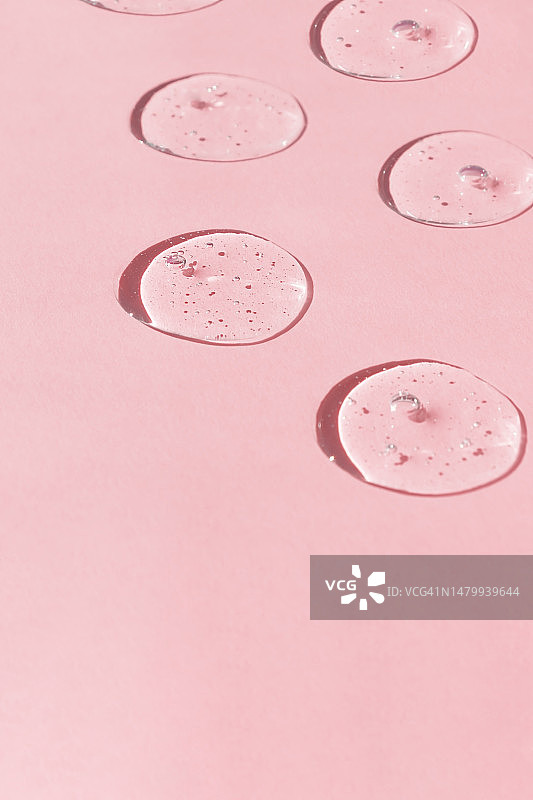 粉色背景上的气泡精华液或透明质酸凝胶：化妆护肤品涂抹图片素材