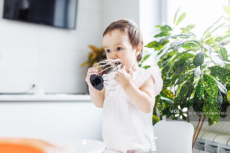在明亮的厨房里品尝搅拌器搅拌的面团的滑稽小女婴图片素材