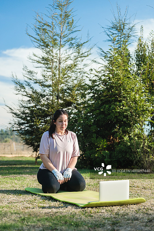 跪在瑜伽垫上，观看电脑瑜伽课程的年轻白人女性图片素材