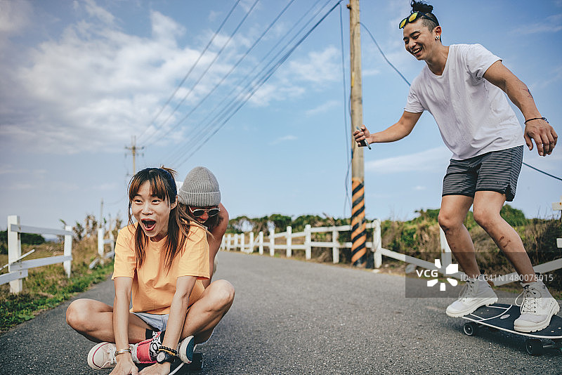 三位亚洲好友户外玩滑板，用手机记录并上传社交媒体图片素材