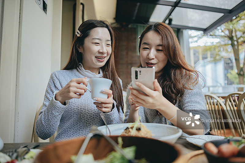 两个女人在咖啡馆分享手机信息，讨论网购或分享新闻，气氛愉快图片素材