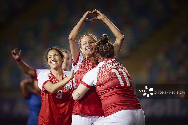 年轻女足球员微笑并用手比心，队友们拥抱她图片素材